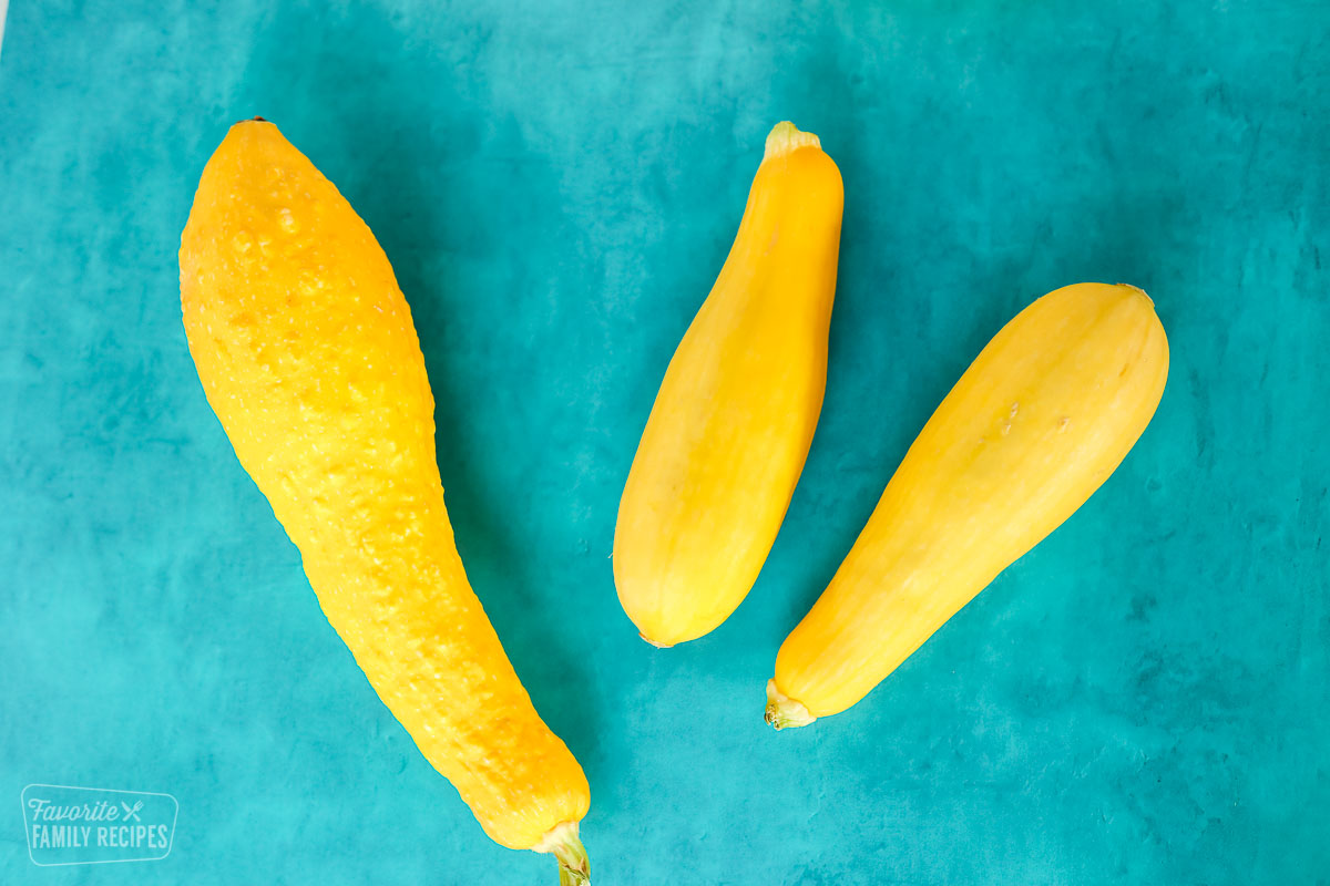 A yellow crookneck squash and two straight neck squash on a table