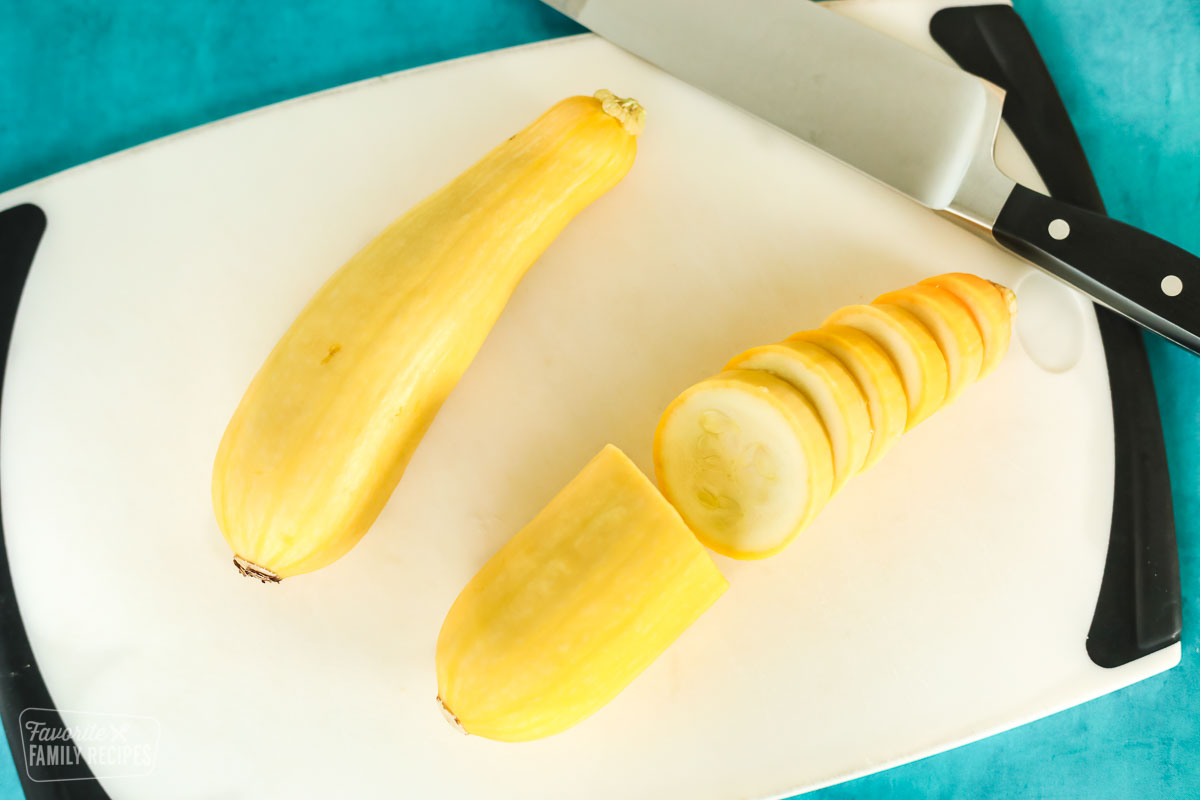 Two yellow Summer squash on a cutting board, one has been sliced half-way through