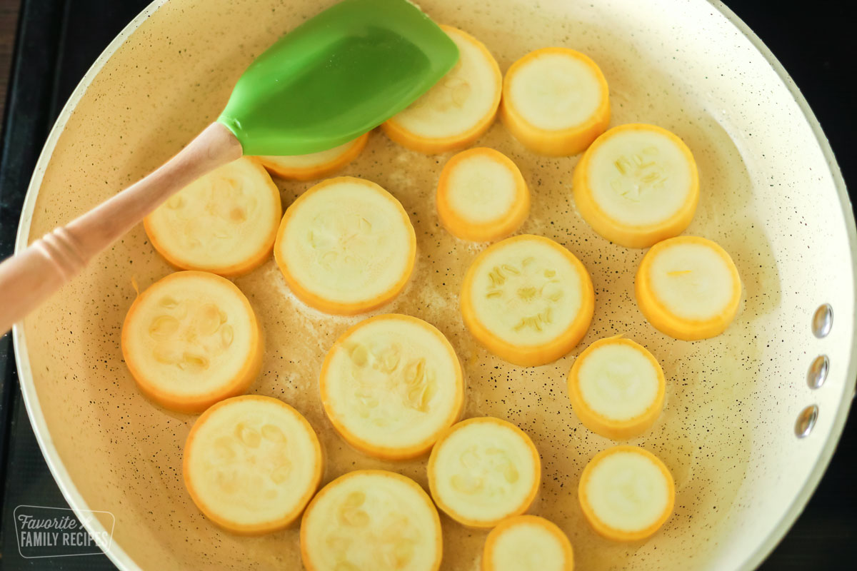 Sliced yellow squash being sautéed in a skillet