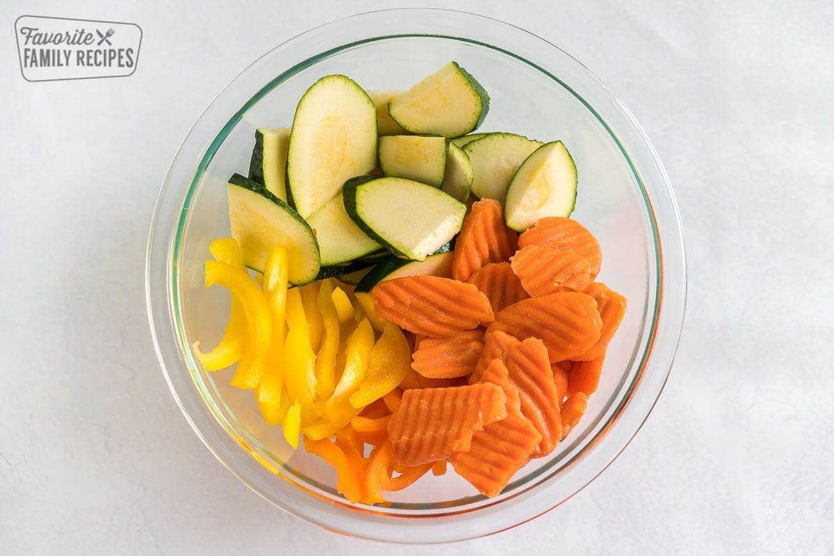 Cut up zucchini, bell peppers, and carrots in a glass bowl