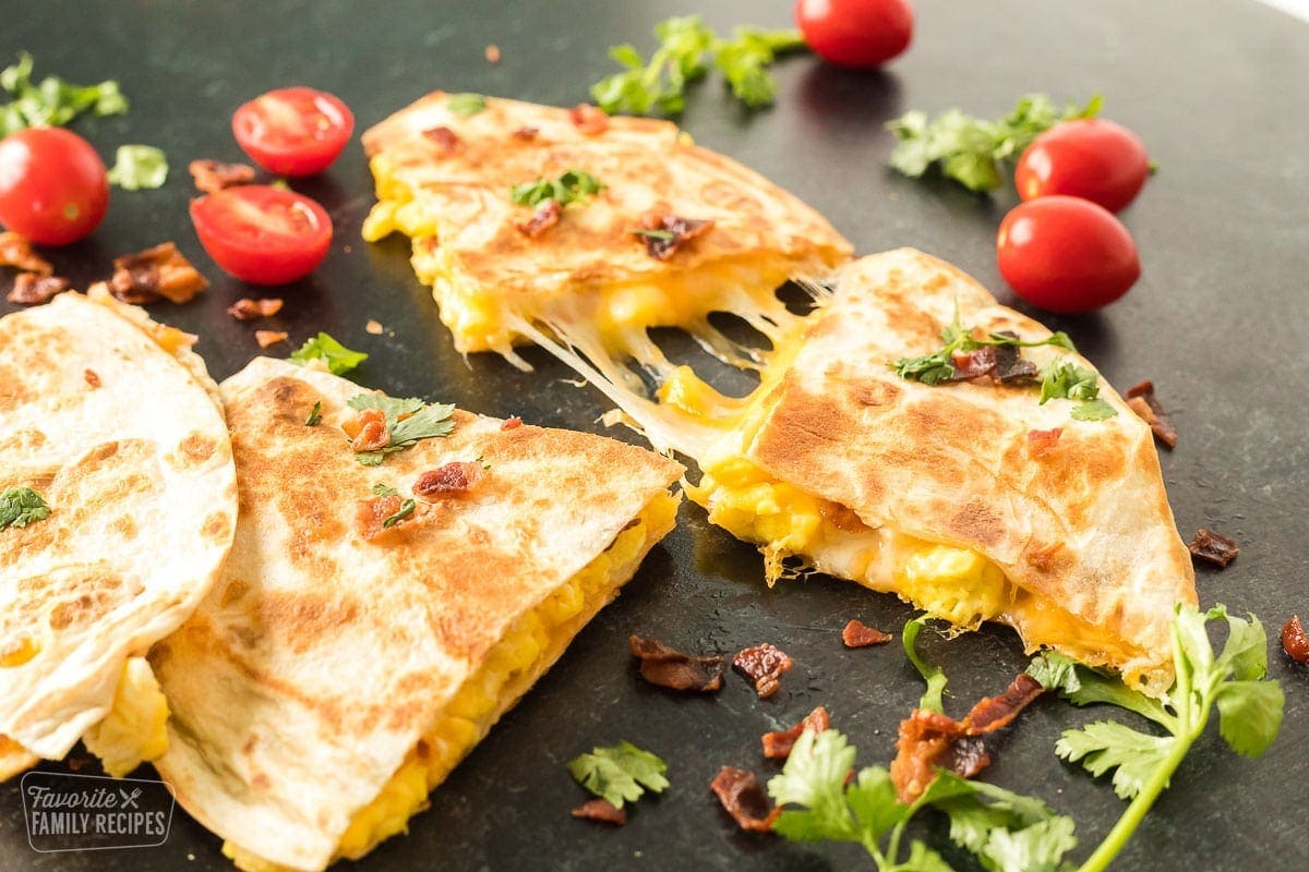 A grilled tortilla stuffed with scrambled eggs, cheese, and bacon being pulled apart to show cheese.