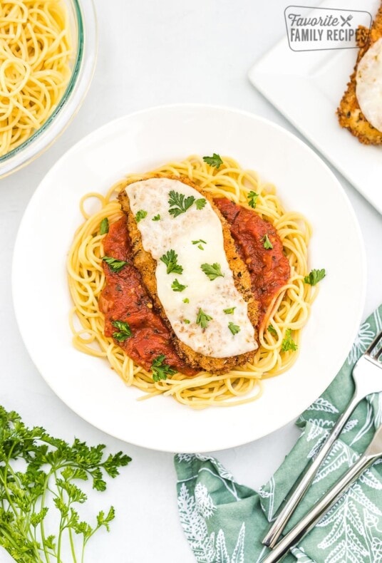 Chicken parmesan laying on top of spaghetti on a white plate.