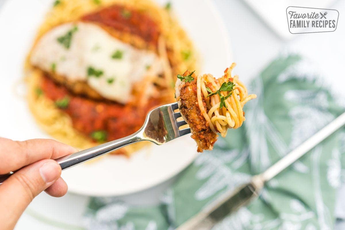 A fork with a piece of chicken and some spaghetti noodles on it.