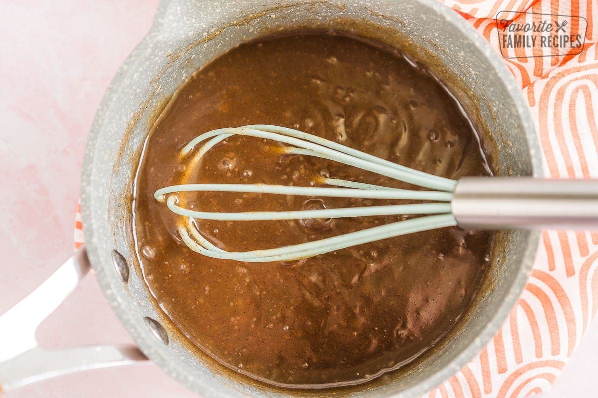 Sauce for peach pie in a saucepan with a whisk in it.