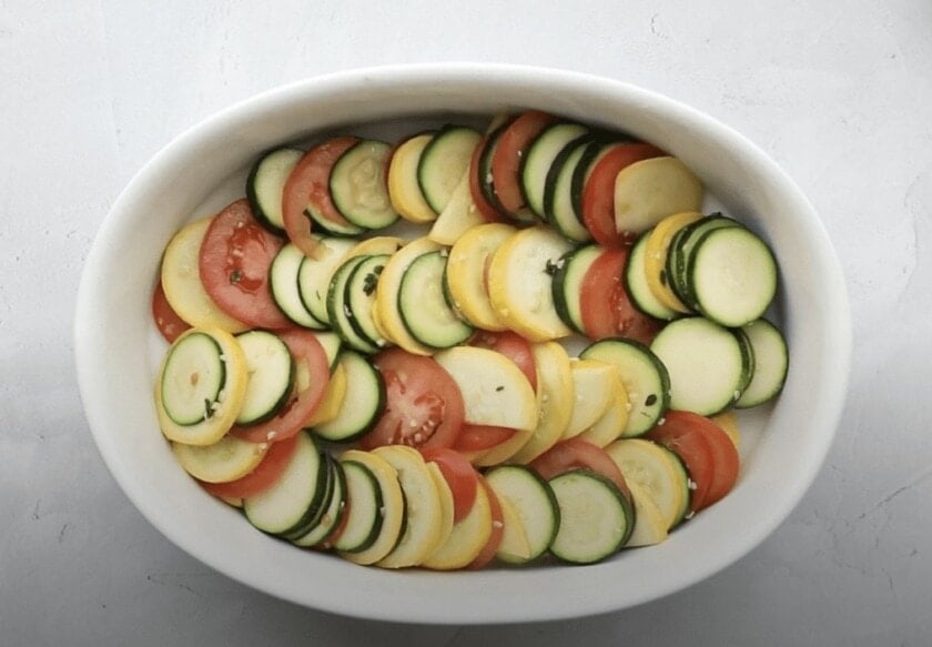 Squash, zucchini, and tomatoes in a single layer in a baking dish.