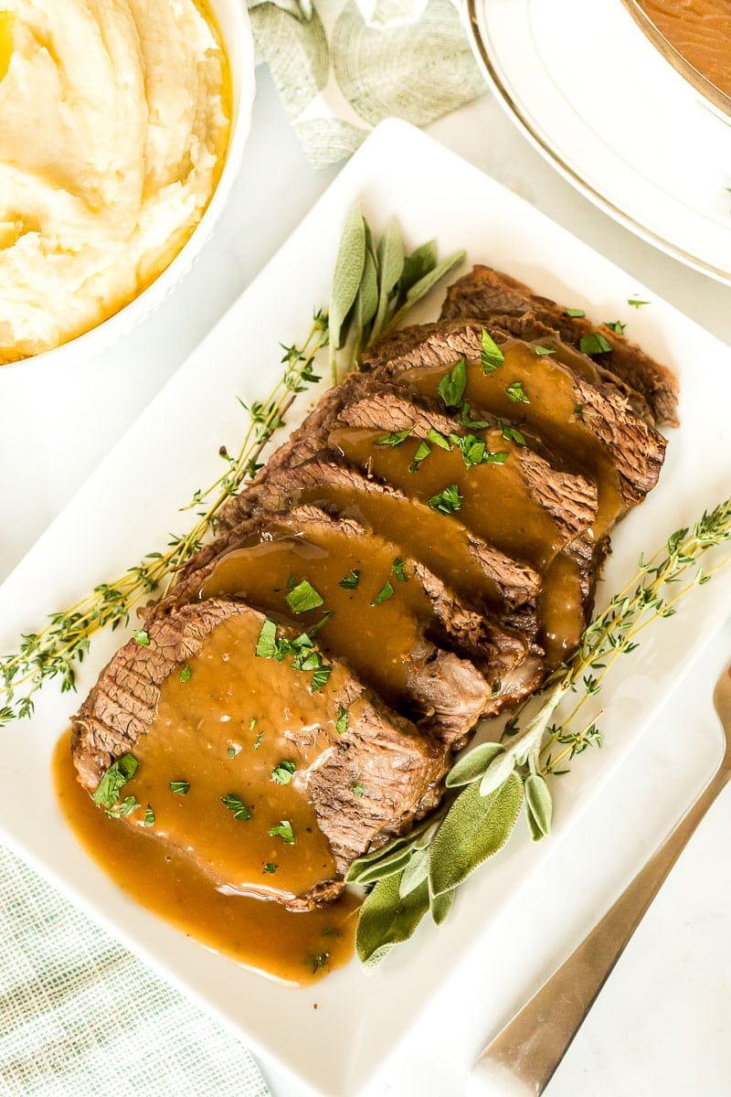 Oven roast beef on a platter with gravy and garnish