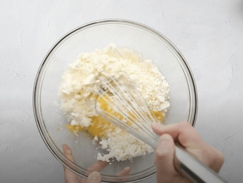 Feta cheese and eggs being mixed in a bowl.