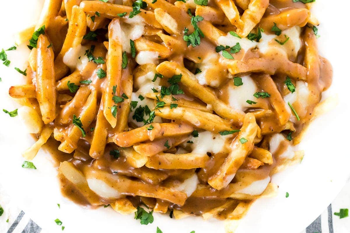 A close up of poutine on a plate with French fries, brown gravy, and cheese curds.