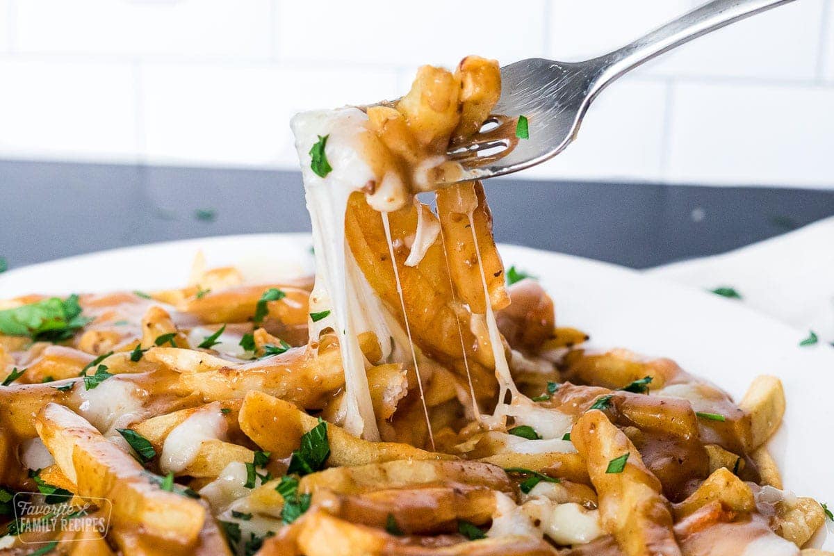 A fork pulling up a bite of poutine with cheese pulling up from the plate.