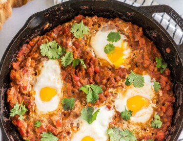 Shakshuka in a cast iron pan with a loaf of bread and cilantro