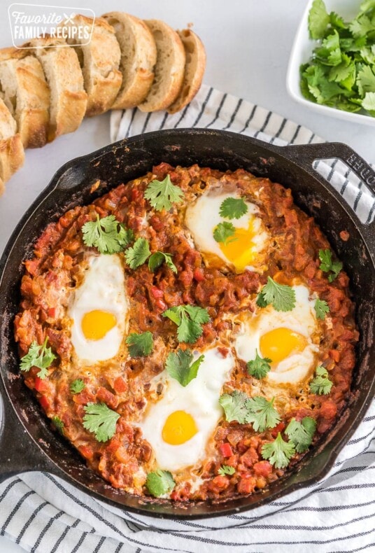 Shakshuka in a cast iron pan with a loaf of bread and cilantro