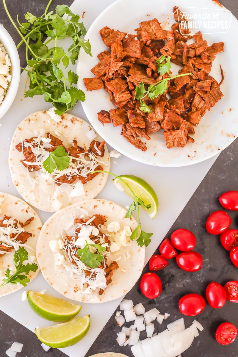 Two street tacos next to a plate of grilled steak