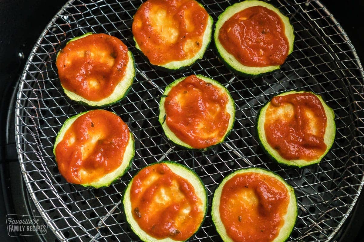 Slices of zucchini with pizza sauce spread over the top