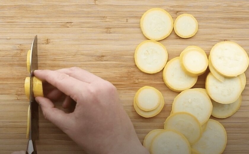 Yellow squash being sliced on a cutting board.