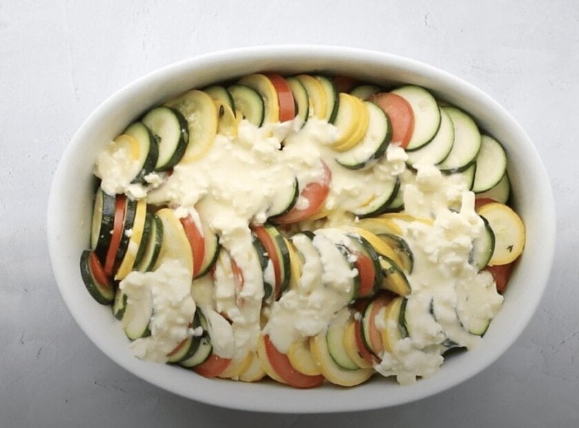 A casserole dish with vegetables with an egg mixture poured over the top.