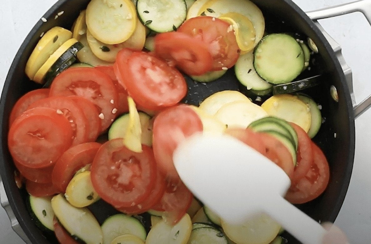 Squash, zucchini, and tomatoes being cooked in a skillet.