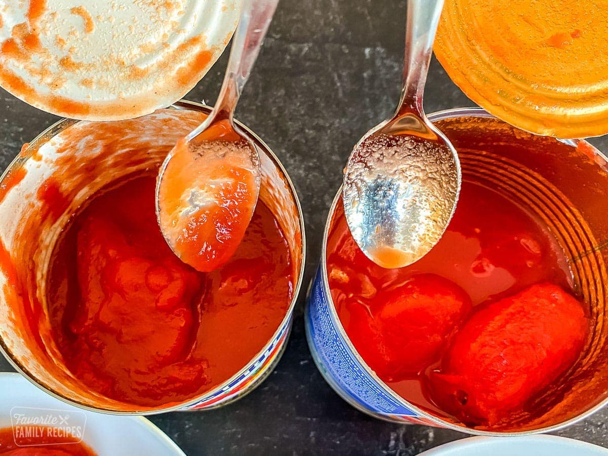 Two spoons dipping into two different cans of tomatoes to show the difference in texture and quality