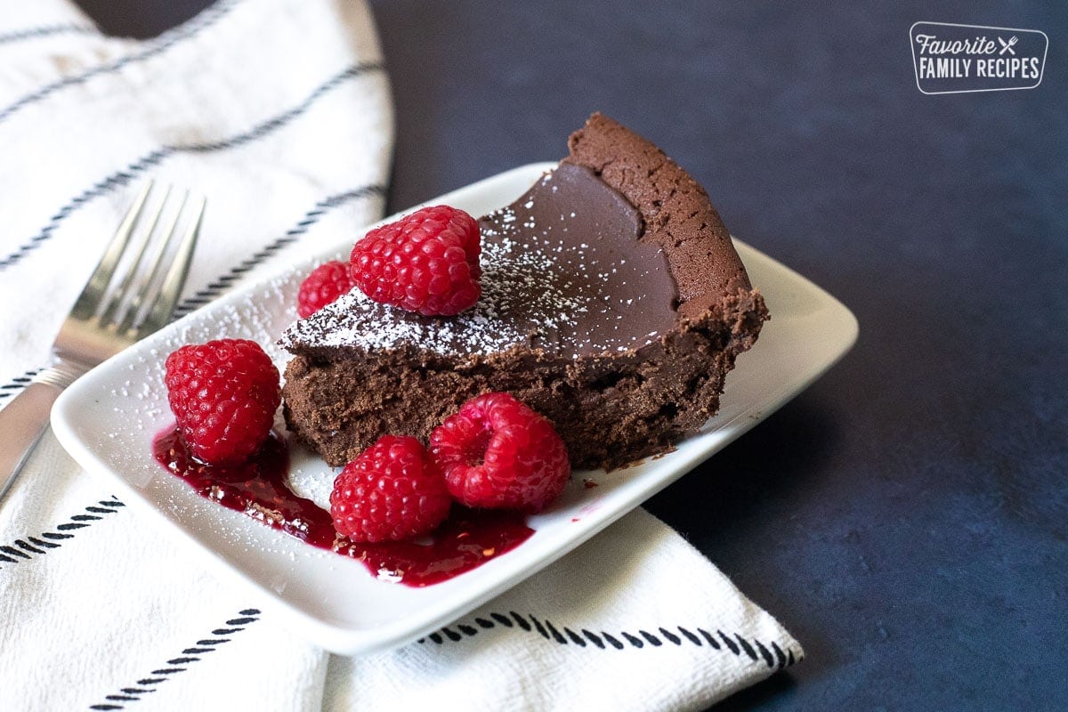 A slice of Flourless Chocolate Cake topped with powdered sugar and raspberries.