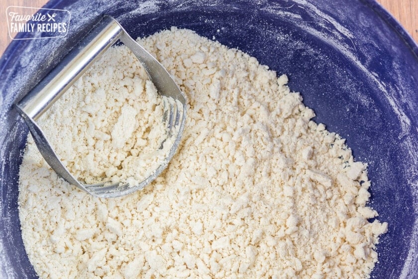 Flour and shortening mixed together in a bowl with a pastry cutter.