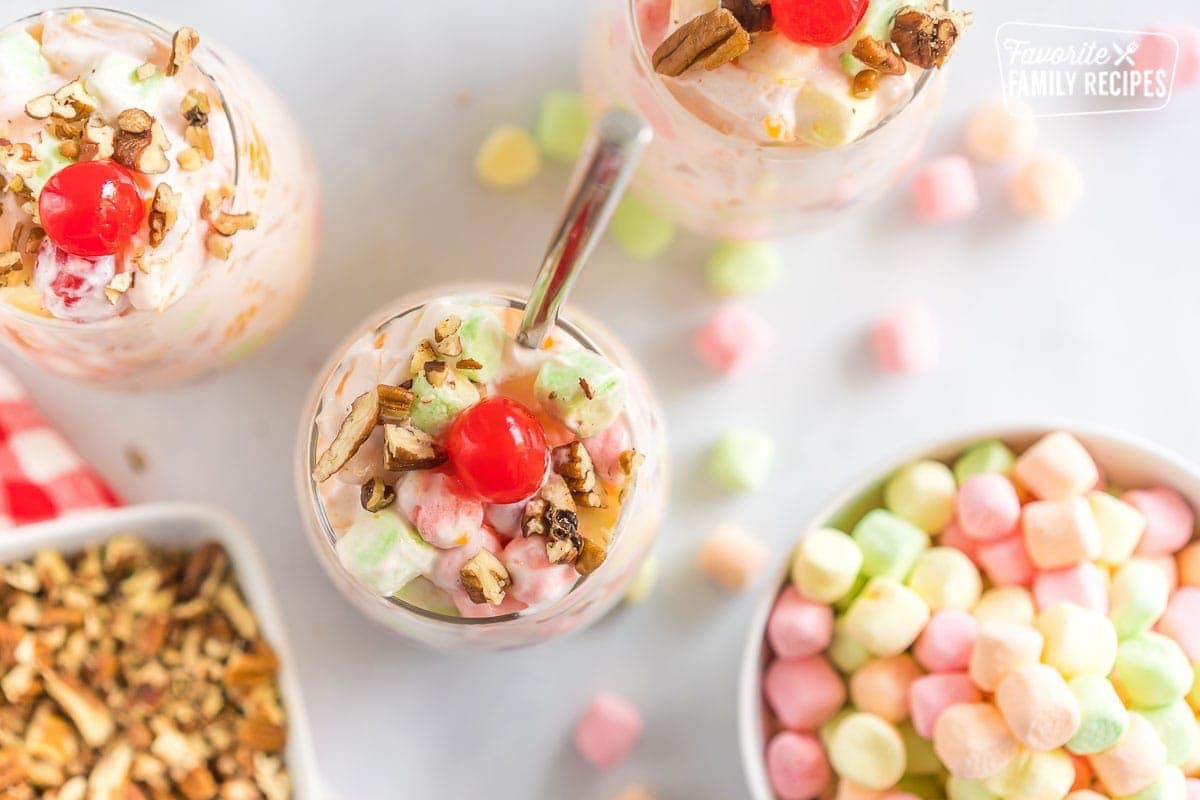 Three cups of Ambrosia salad topped with pecans and cherries