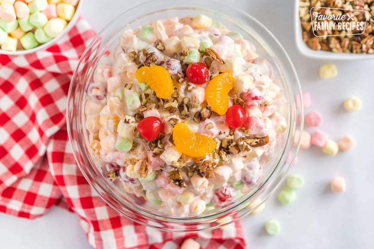 A large bowl of ambrosia salad topped with orange slices, maraschino cherries, and pecans.