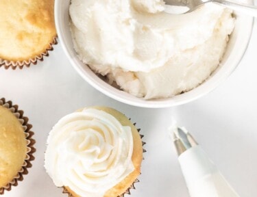 A bowl of buttercream frosting next to some cupcakes