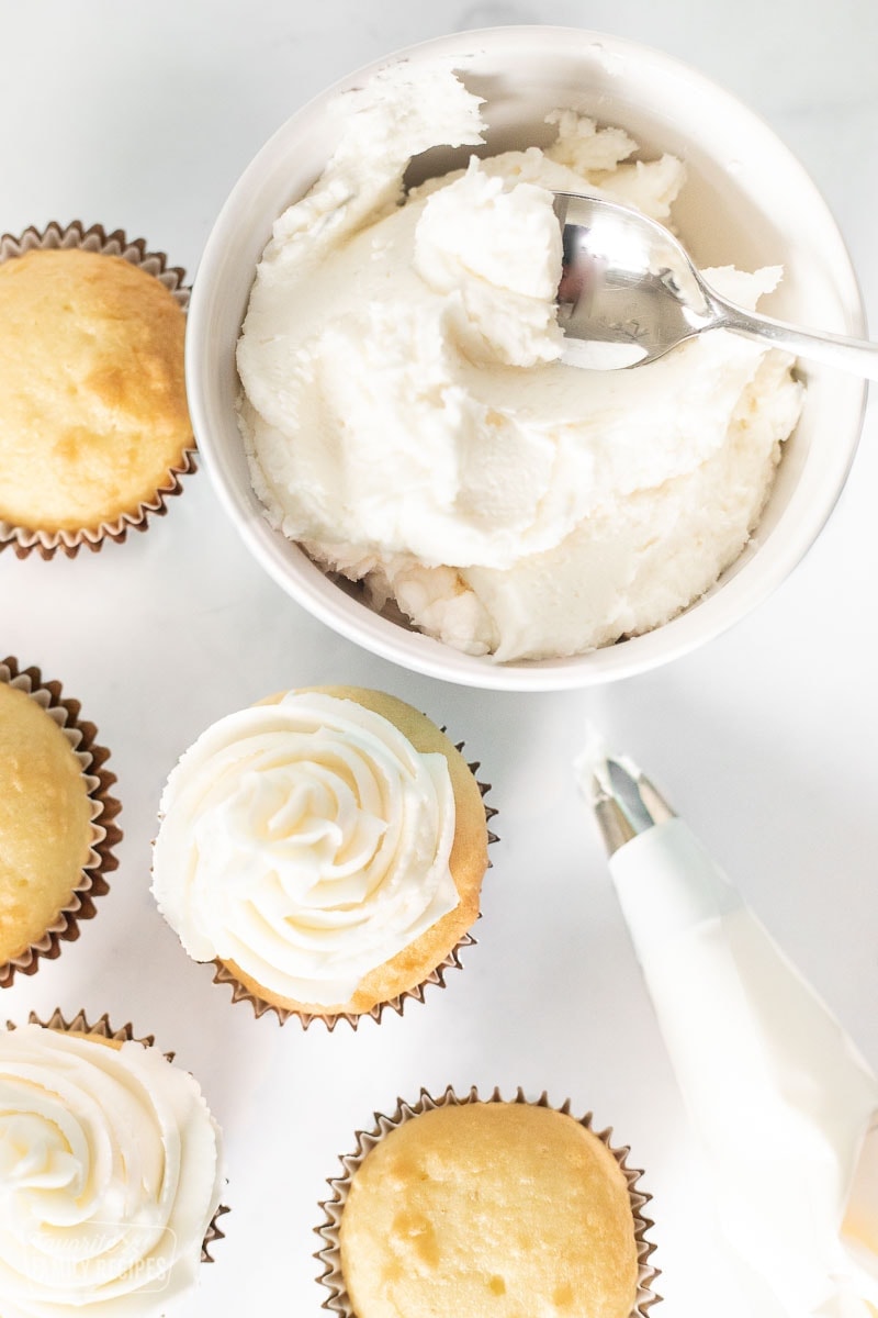 A bowl of buttercream frosting next to some cupcakes