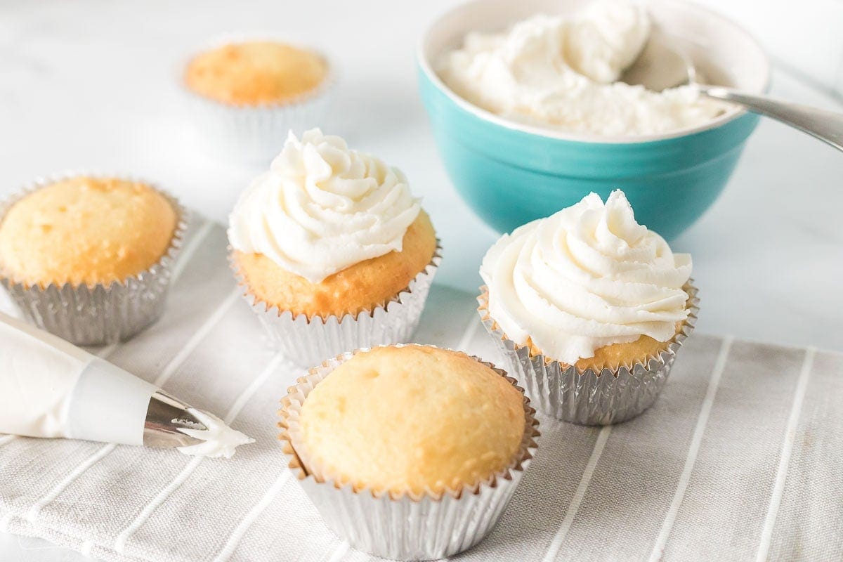 A piping bag with frosting, five cupcakes, and a bowl of frosting
