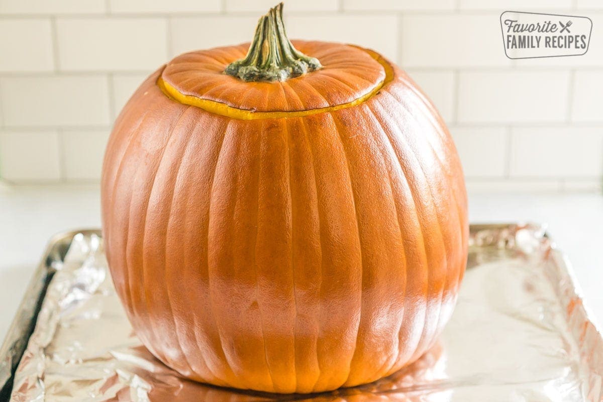 A pumpkin with the top cut out on a baking sheet with aluminum foil. 