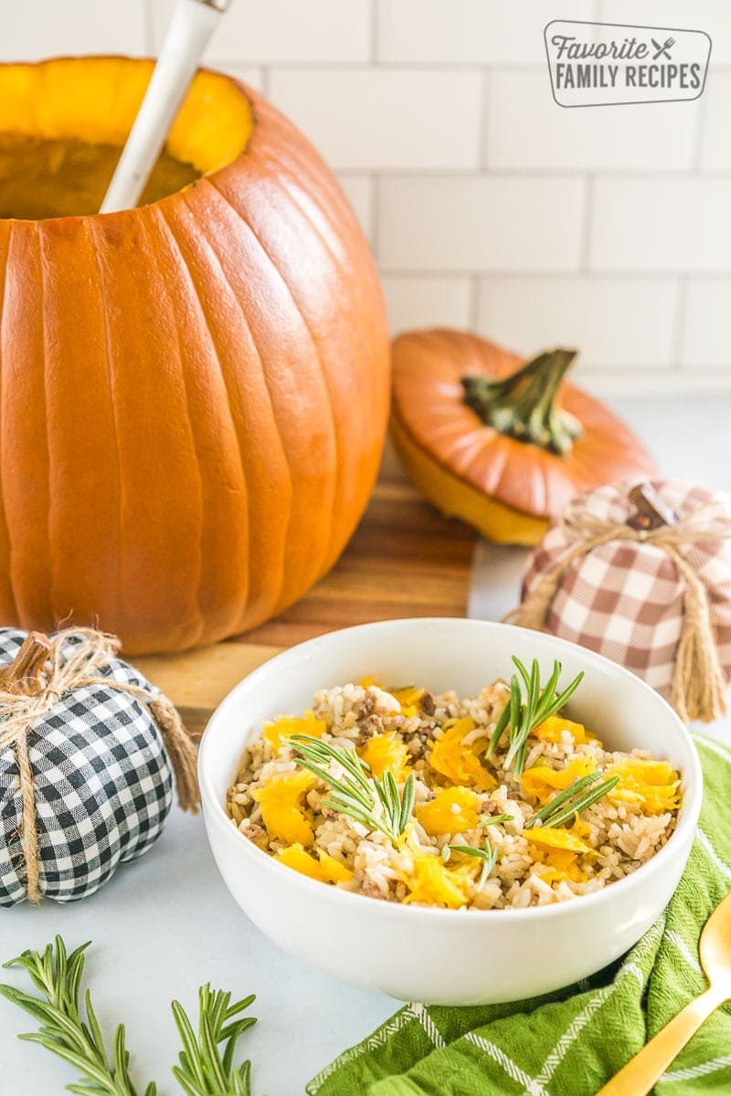 A large pumpkin filled with casserole and a bowl with casserole topped with pumpkin chunks and fresh rosemary