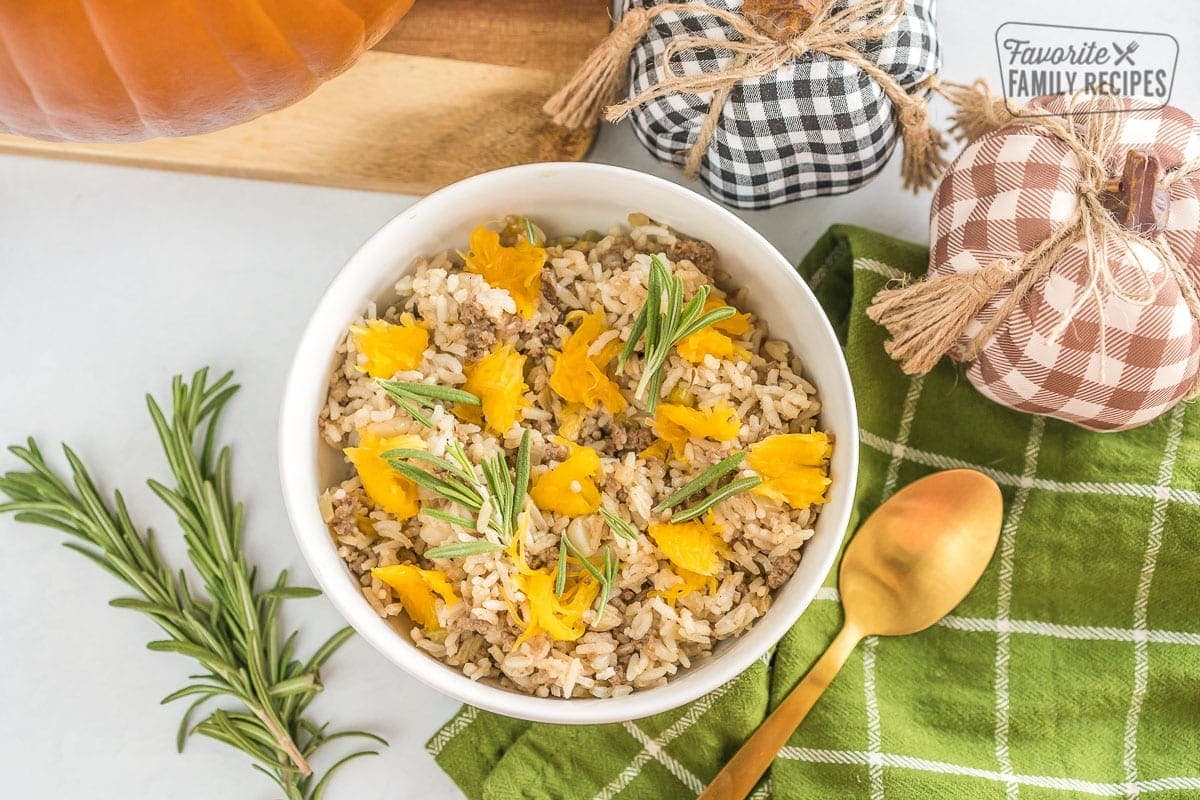 A bowl of dinner in a pumpkin casserole topped with fresh rosemary.