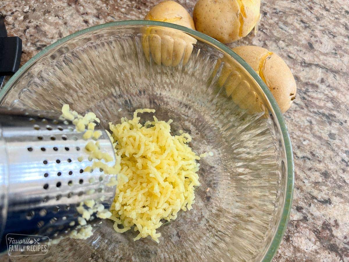 Yellow potatoes being riced into a large glass bowl.