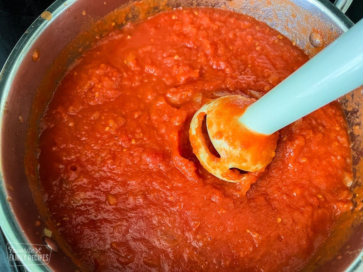 Tomatoes being blended into a sauce with an immersion blender