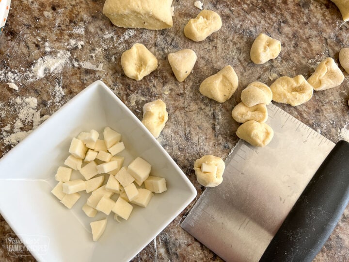 Dough cut in pieces to make gnocchi next to a bowl of cut mozzarella