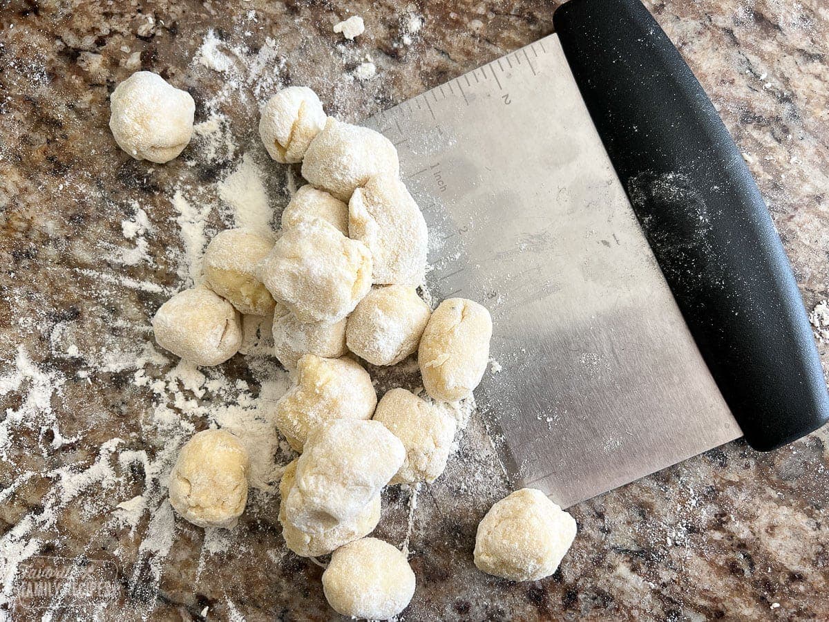 A bench scraper next to balls of uncooked gnocchi.