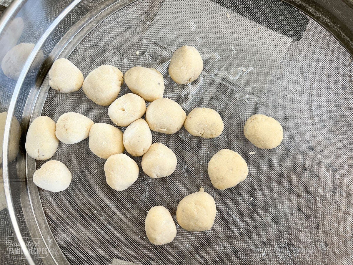 Gnocchi dough balls being rolled in a sieve.