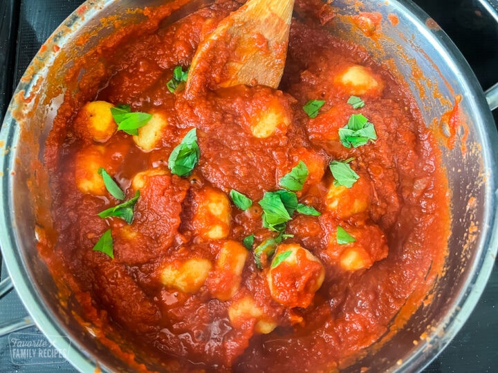 A skillet with tomato sauce with gnocchi being stirred in