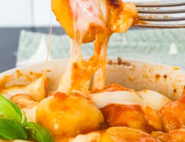 Gnocchi with tomato sauce in a soufflé dish. A fork is pulling up some of the gnocchi from the dish.