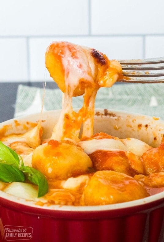 Gnocchi with tomato sauce in a soufflé dish. A fork is pulling up some of the gnocchi from the dish.