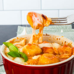 Gnocchi with tomato sauce in a soufflé dish. A fork is pulling up some of the gnocchi from the dish.