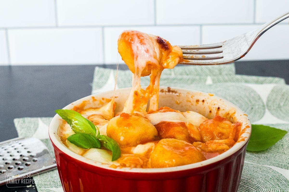 Gnocchi with tomato sauce in a soufflé dish. A fork is pulling up some of the gnocchi from the dish.
