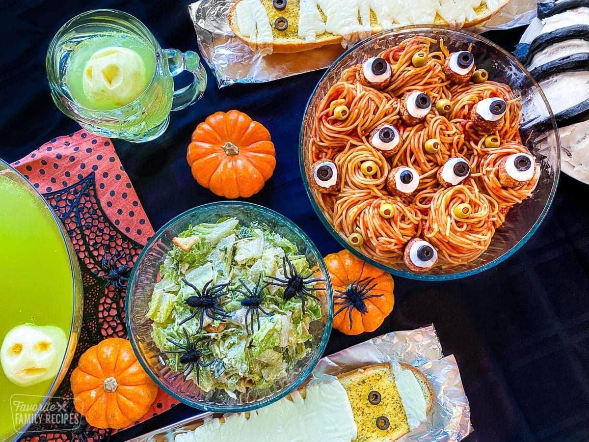 Spaghetti with meatballs that have cheese and olives that look like eyes, green punch, French bread with cheese, and a Caesar salad with plastic spiders for a Halloween dinner.