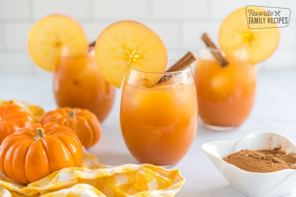 A glass of pumpkin juice topped with an apple slice and a cinnamon stick