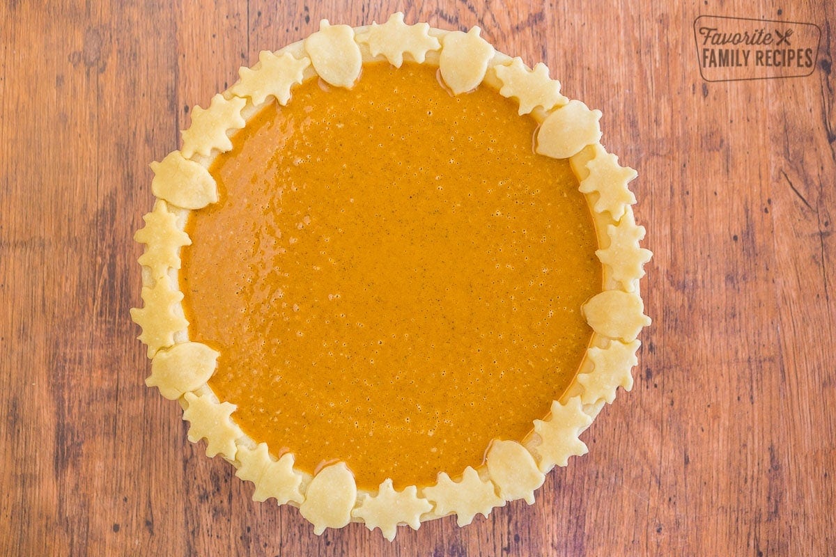 An unbaked pumpkin pie with maple leaf and acorn decorations around the outside