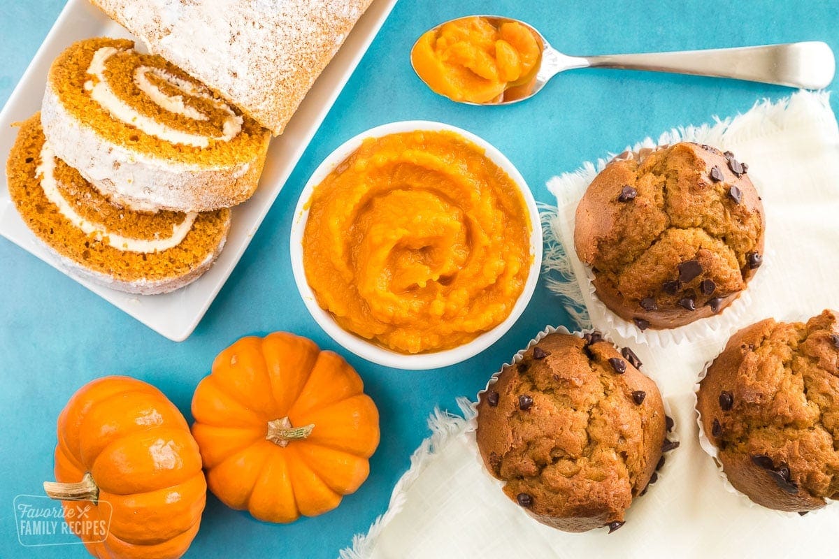 Pumpkin puree in a bowl next to pumpkin muffins and a pumpkin roll.