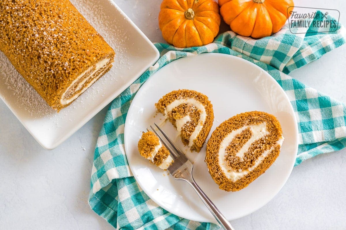 Two slices of pumpkin roll on a plate with a bite taken out of one.