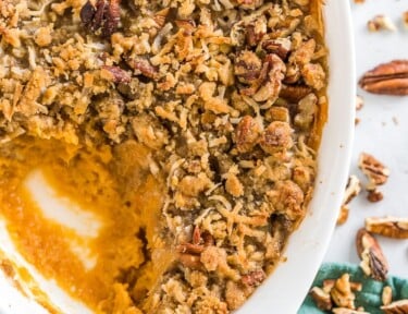 A close up of a sweet potato casserole with pecan topping in a baking dish with a scoop out of the casserole