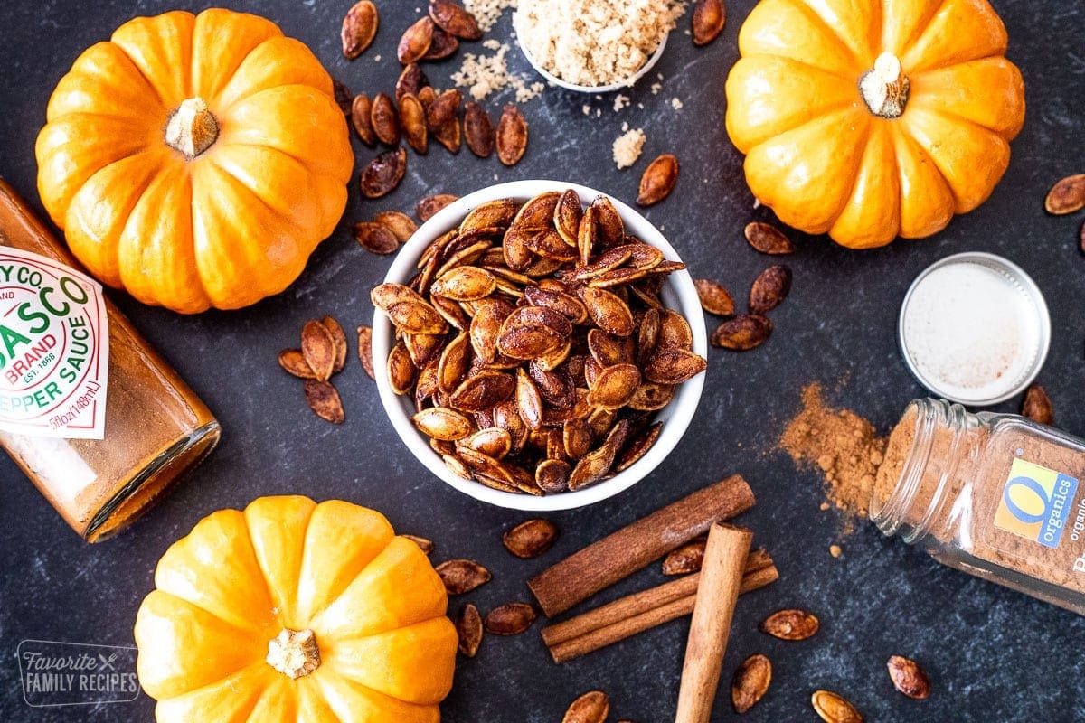 Sweet and spicy pumpkin seeds in a bowl next to pumpkins