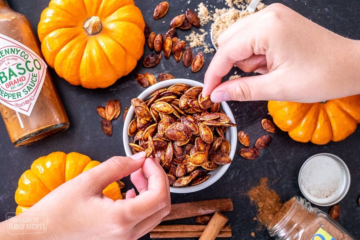 Pumpkin seeds in a bowl with two hands picking out the seeds