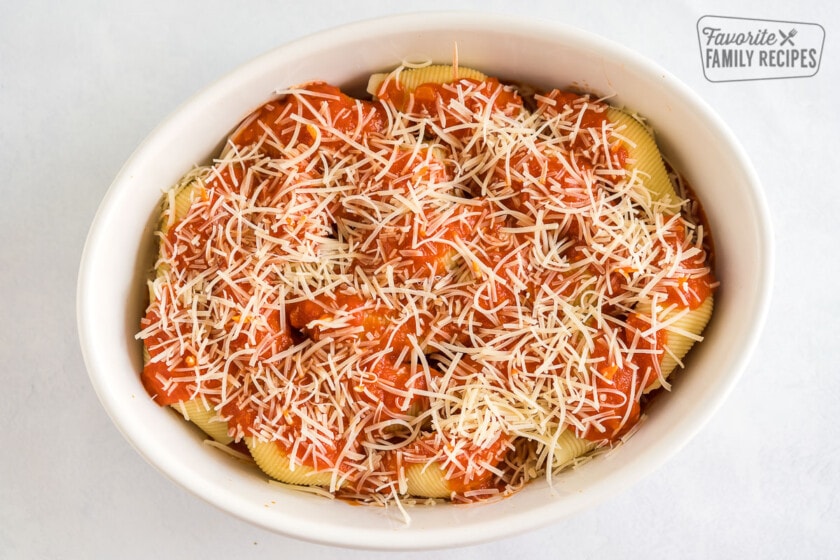 A casserole dish with uncooked Chicken Parmesan Stuffed Shells covered in a tomato sauce and shredded cheese.